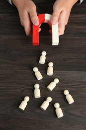 Photo of Man with magnet attracting human figures at wooden table, above view