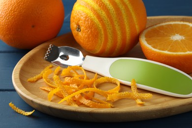 Photo of Plate with orange zest, fresh fruit and zester on blue wooden table, closeup