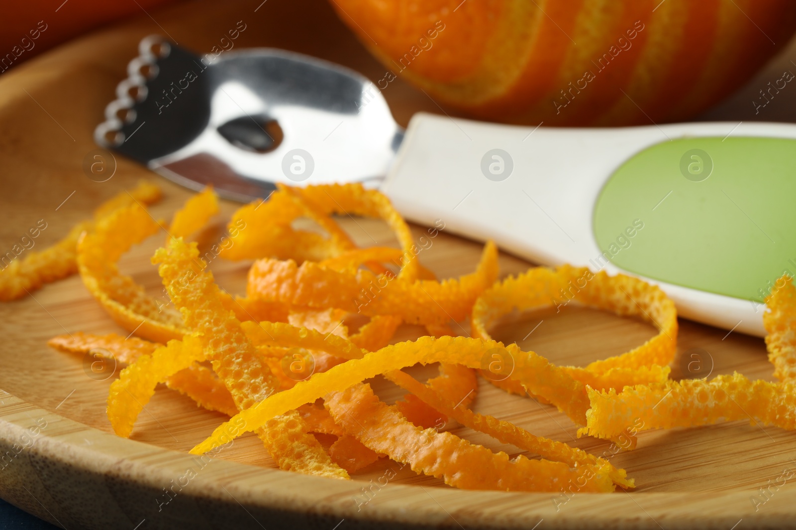 Photo of Fresh orange zest, fruit and zester on wooden plate, closeup