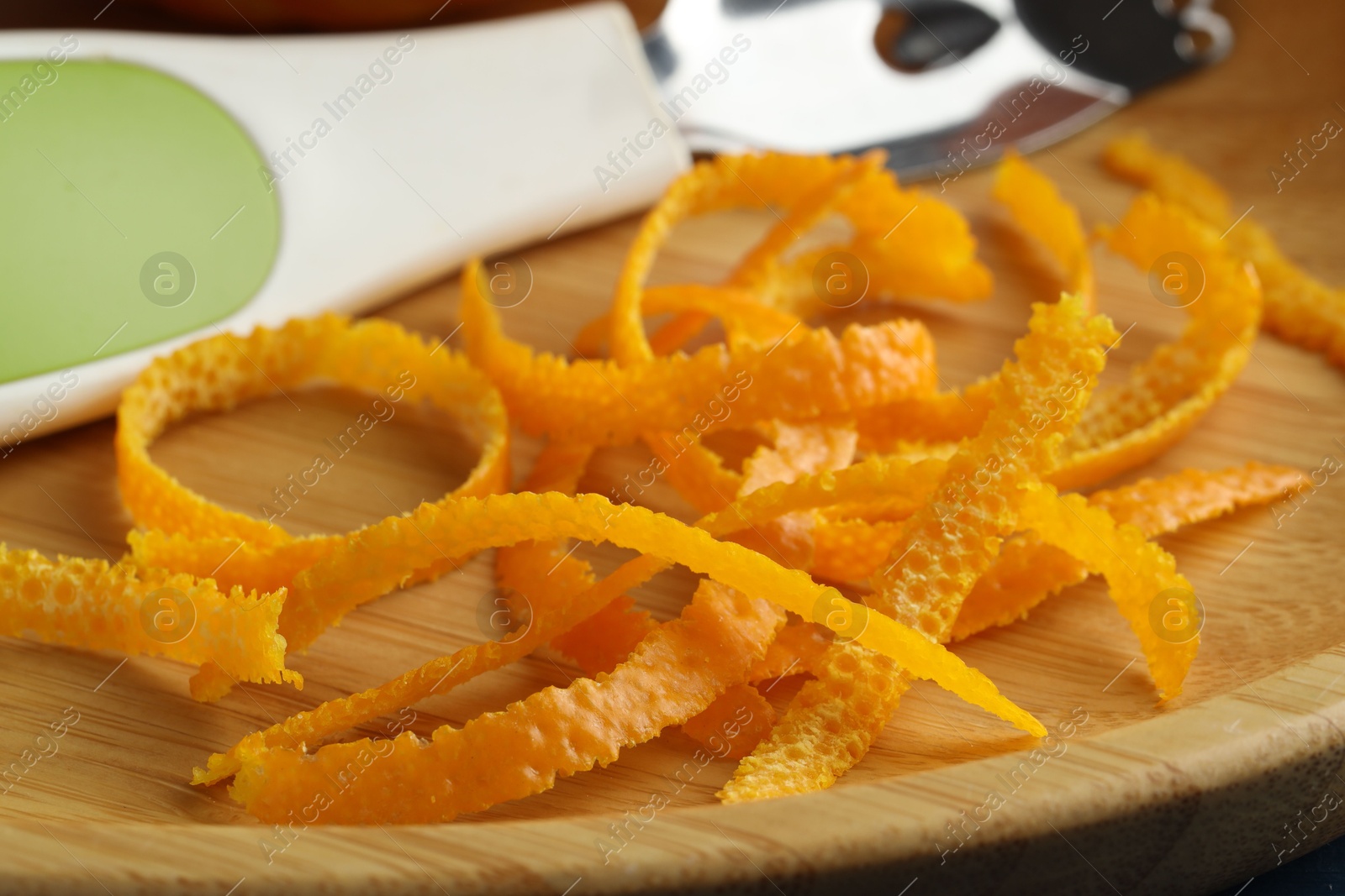 Photo of Fresh orange zest and zester on wooden plate, closeup