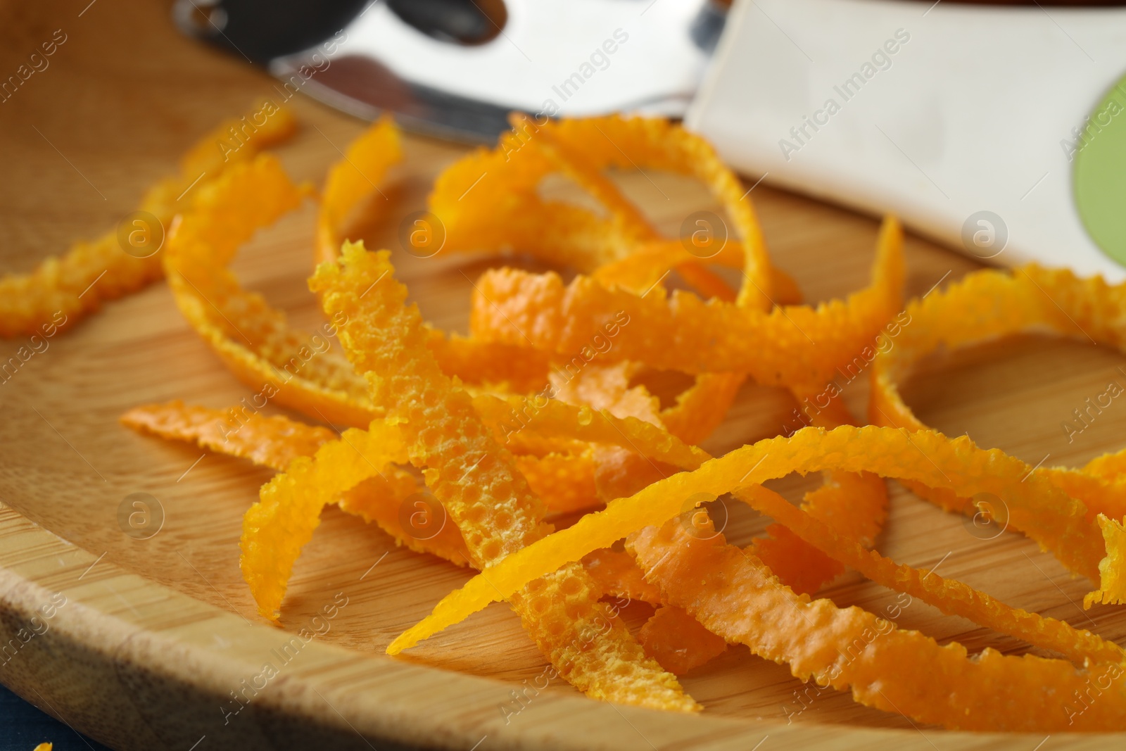 Photo of Fresh orange zest and zester on wooden plate, closeup