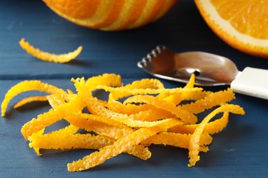 Photo of Fresh orange zest, fruits and zester on blue wooden table, closeup