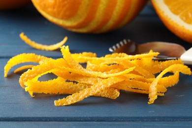 Photo of Fresh orange zest, fruits and zester on blue wooden table, closeup