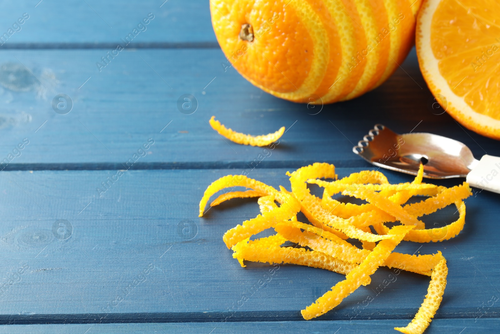 Photo of Fresh orange zest, fruits and zester on blue wooden table, closeup. Space for text