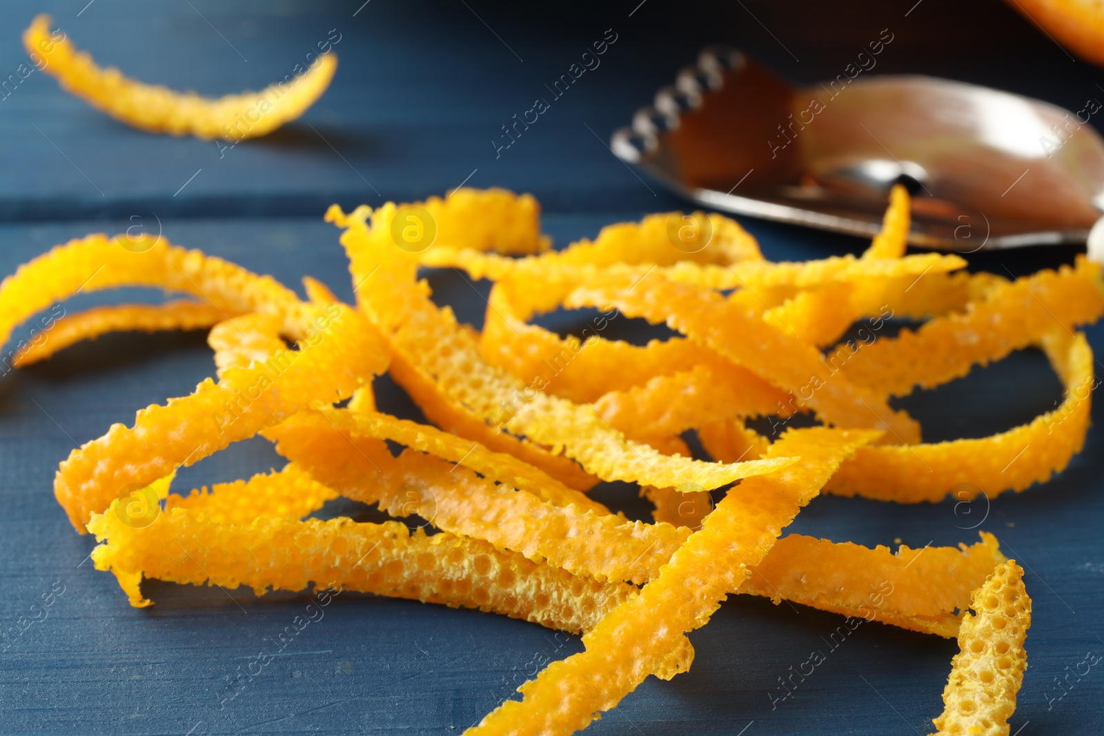 Photo of Fresh orange zest and zester on blue wooden table, closeup