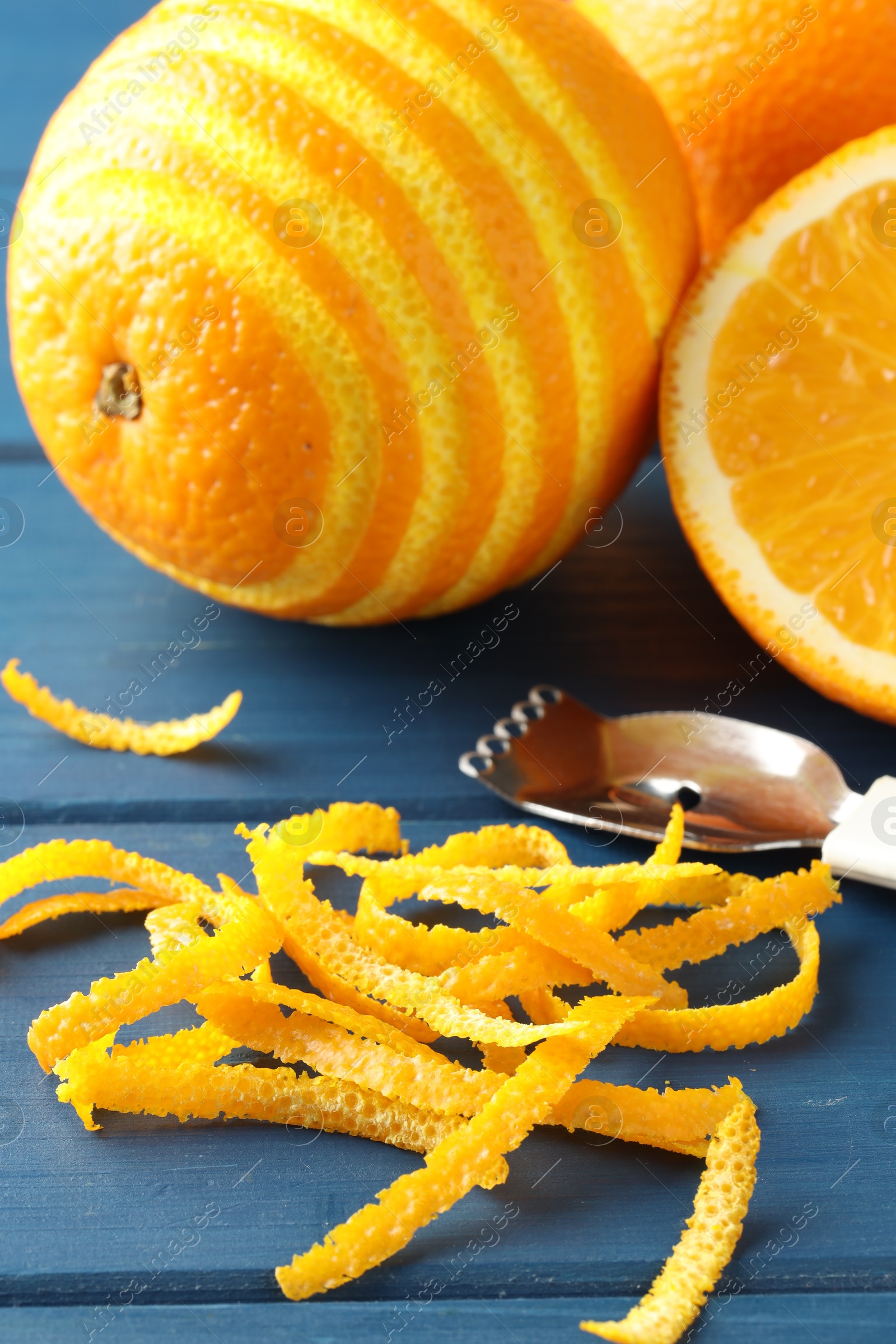 Photo of Fresh orange zest, fruits and zester on blue wooden table, closeup