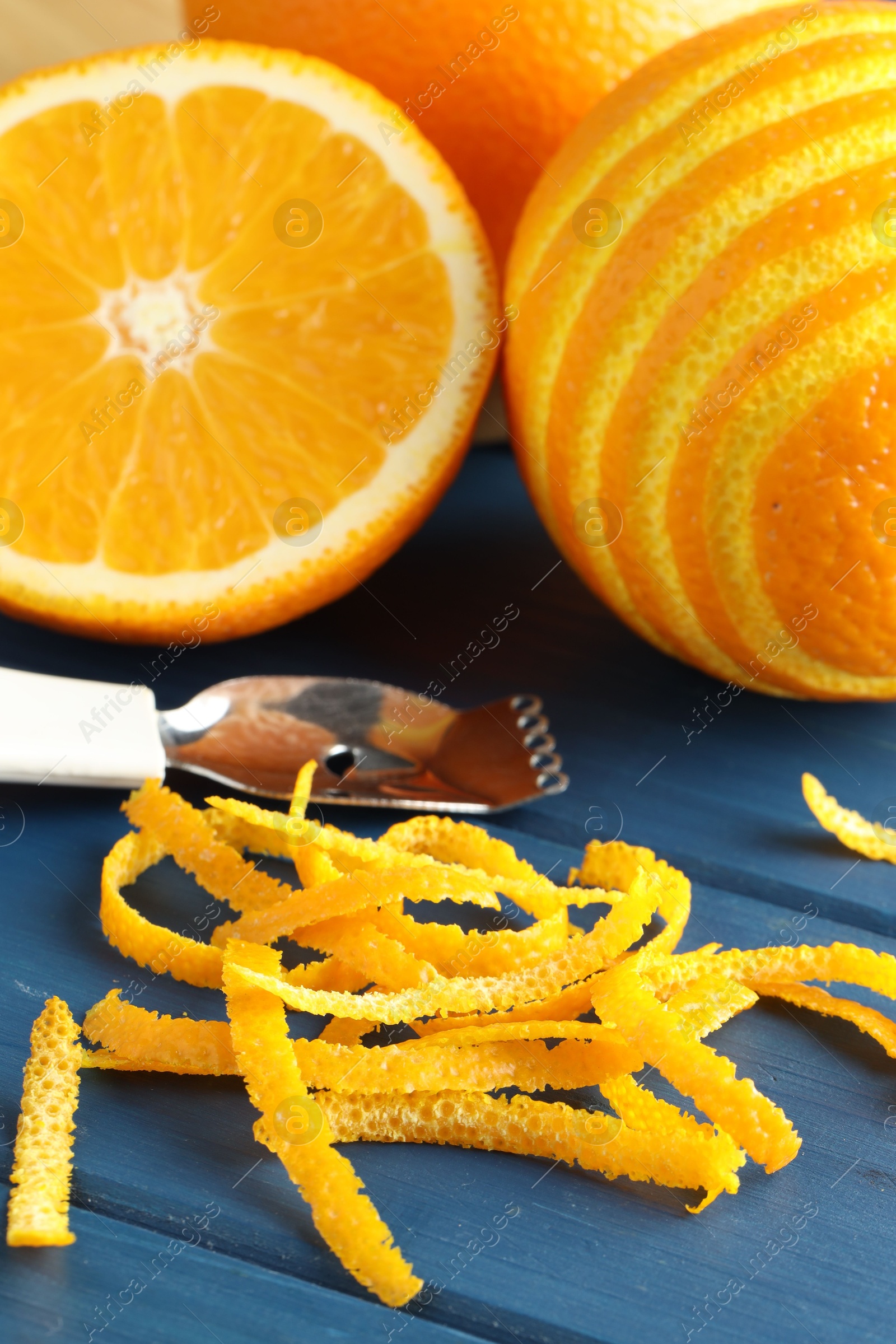 Photo of Fresh orange zest, fruits and zester on blue wooden table, closeup