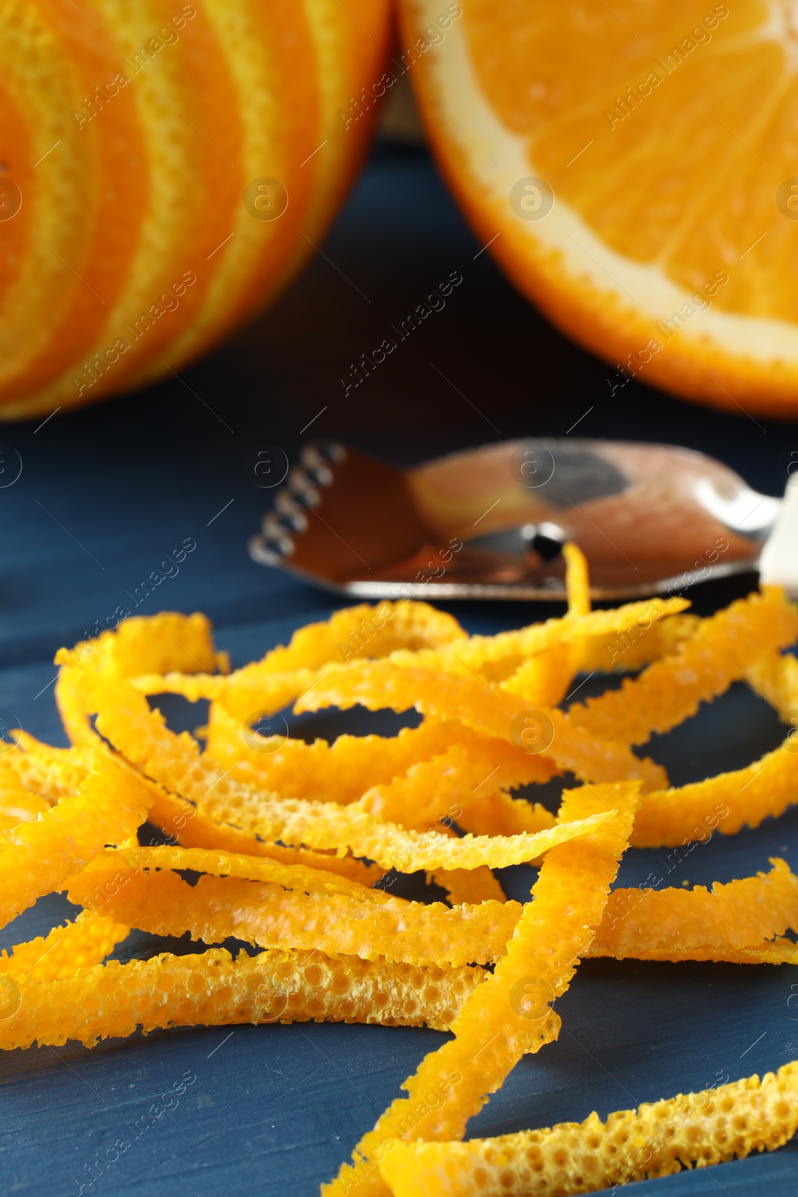 Photo of Fresh orange zest, fruits and zester on blue wooden table, closeup