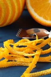 Photo of Fresh orange zest, fruits and zester on blue wooden table, closeup