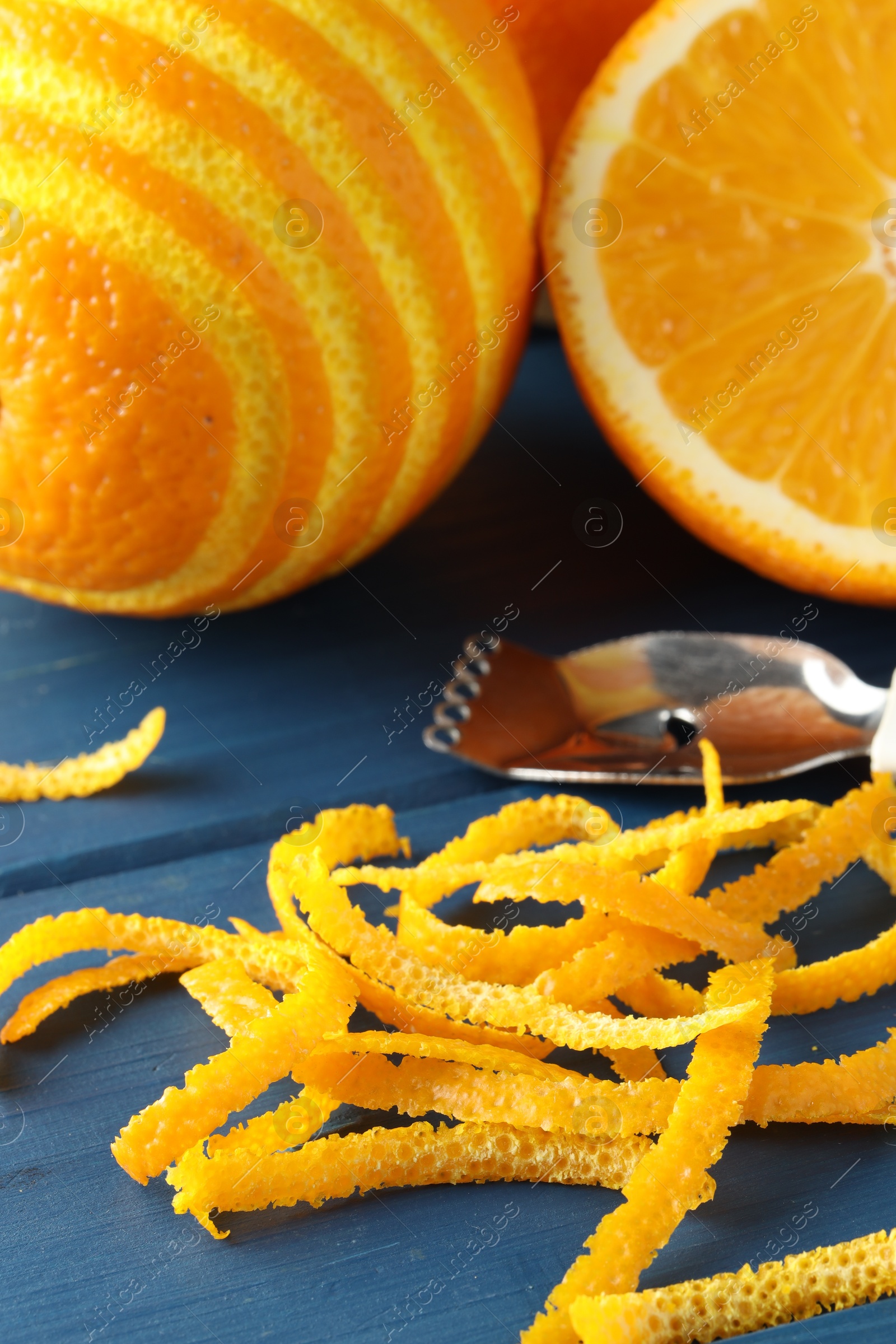 Photo of Fresh orange zest, fruits and zester on blue wooden table, closeup