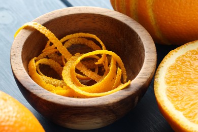 Photo of Bowl with fresh orange zest and fruits on blue wooden table, closeup