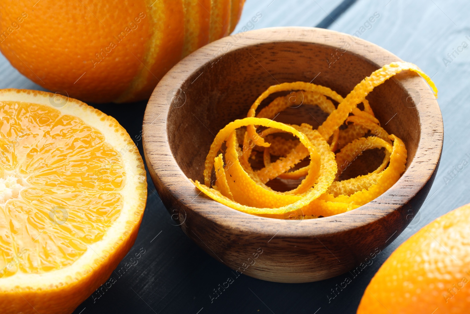 Photo of Bowl with fresh orange zest and fruits on blue wooden table, closeup