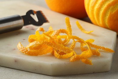 Photo of Fresh orange zest, fruits and zester on light textured table, closeup