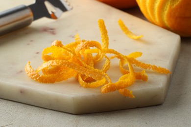 Photo of Fresh orange zest, fruit and zester on light textured table, closeup