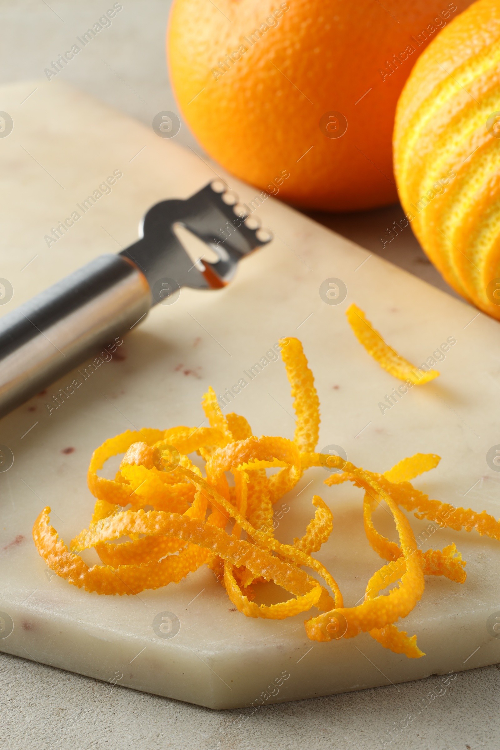 Photo of Fresh orange zest, fruits and zester on light textured table, closeup