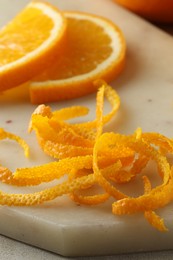 Photo of Fresh orange zest and slices of fruit on light textured table, closeup