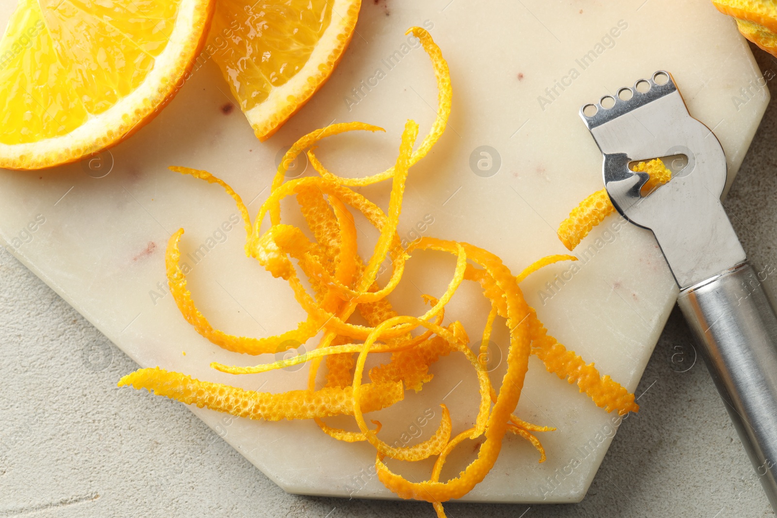 Photo of Fresh orange zest, slices of fruit and zester on light textured table, flat lay