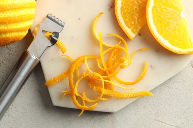 Photo of Fresh orange zest, slices of fruit and zester on light textured table, flat lay