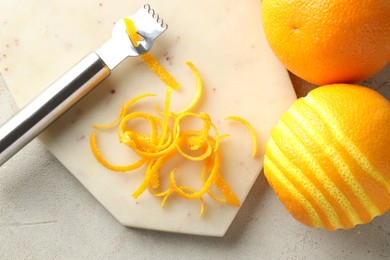 Fresh orange zest, fruits and zester on light textured table, flat lay