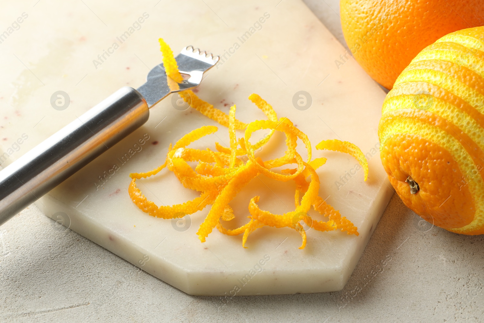 Photo of Fresh orange zest, fruits and zester on light textured table, closeup