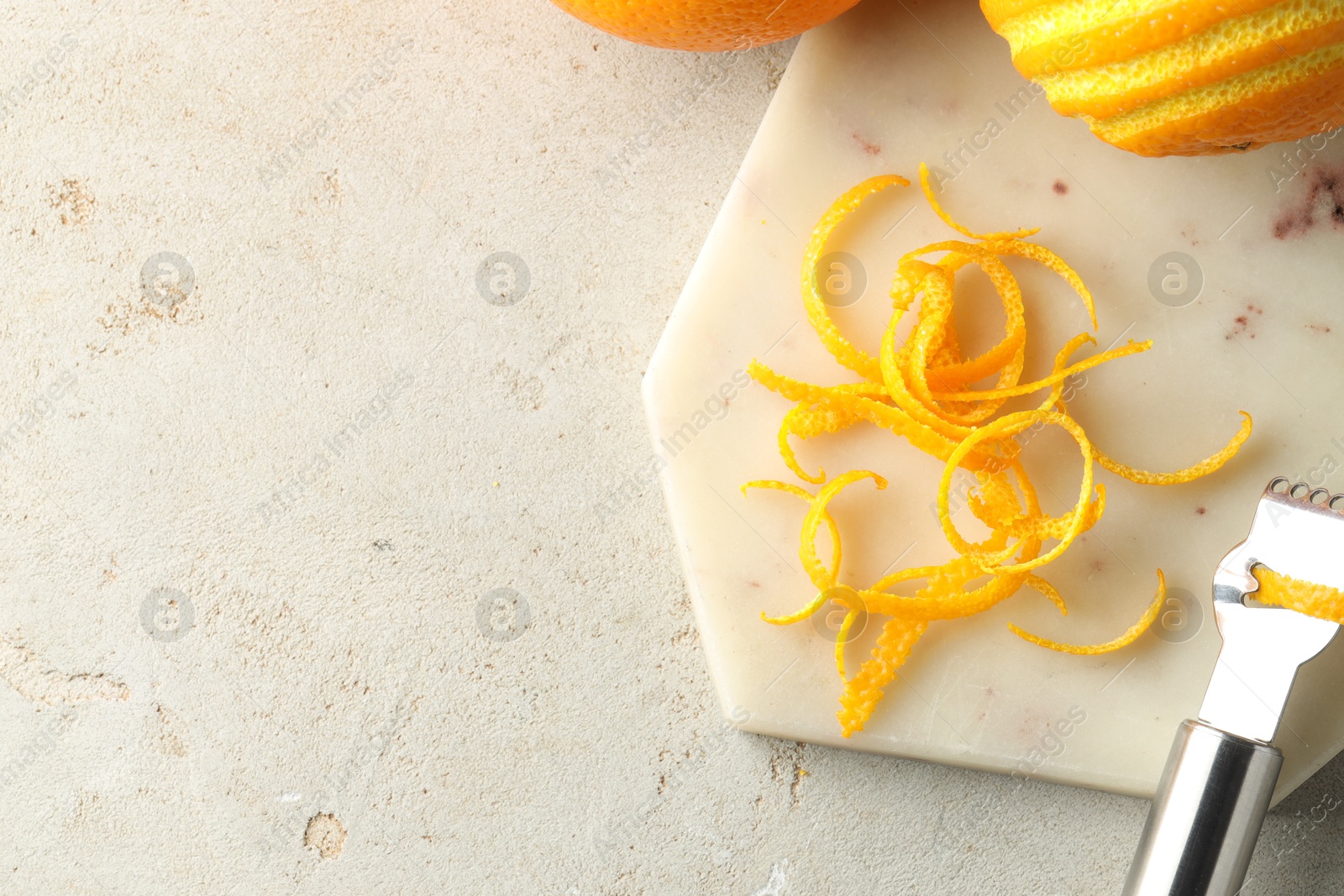 Photo of Fresh orange zest, fruits and zester on light textured table, flat lay. Space for text