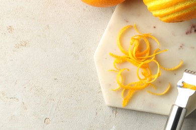 Photo of Fresh orange zest, fruits and zester on light textured table, flat lay. Space for text