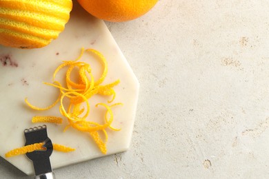 Photo of Fresh orange zest, fruits and zester on light textured table, flat lay. Space for text