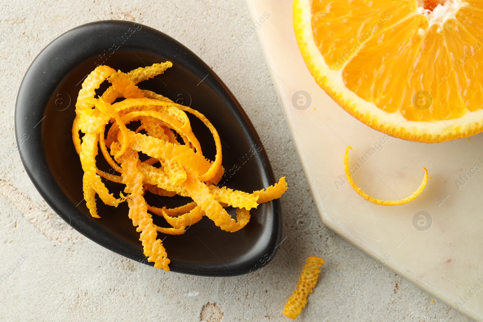 Photo of Fresh orange zest and half of fruit on light textured table, flat lay