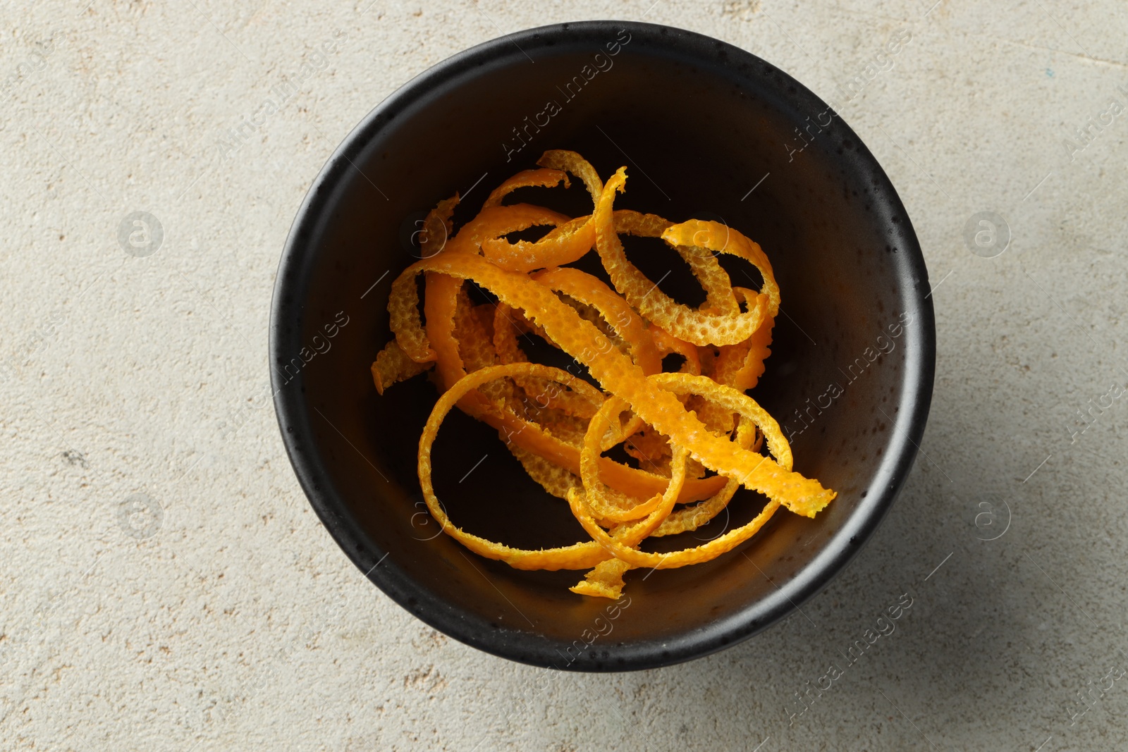 Photo of Fresh orange zest in bowl on light textured table, top view