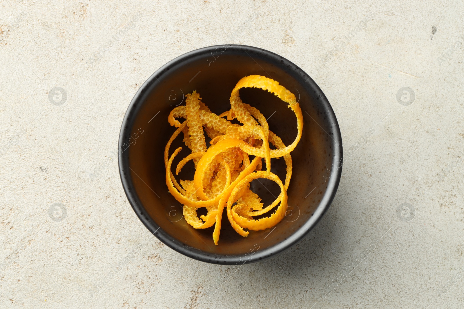 Photo of Fresh orange zest in bowl on light textured table, top view