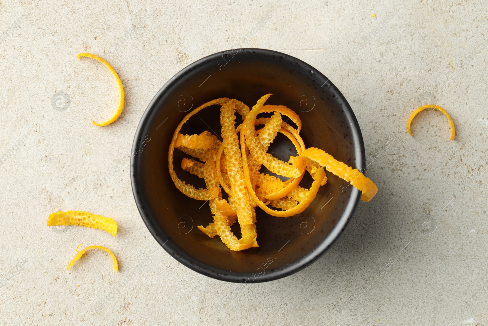 Photo of Fresh orange zest in bowl on light textured table, flat lay