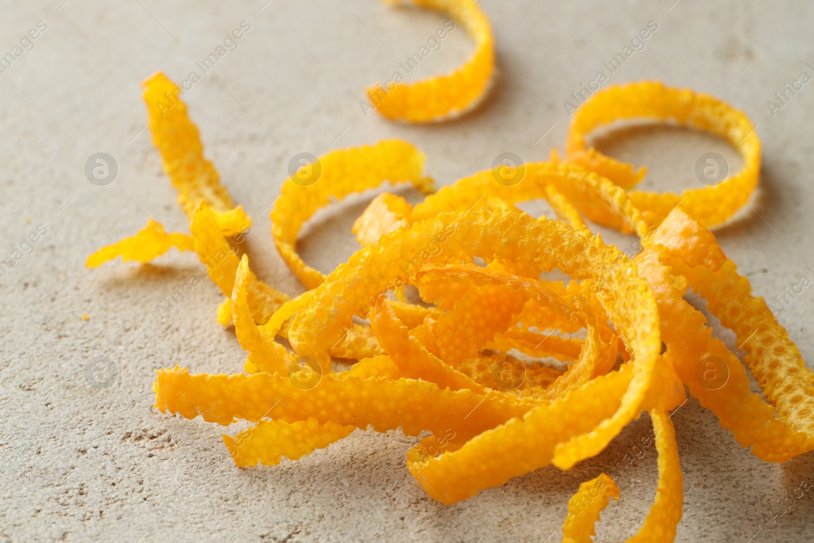 Photo of Pile of fresh orange zest on light textured table, closeup