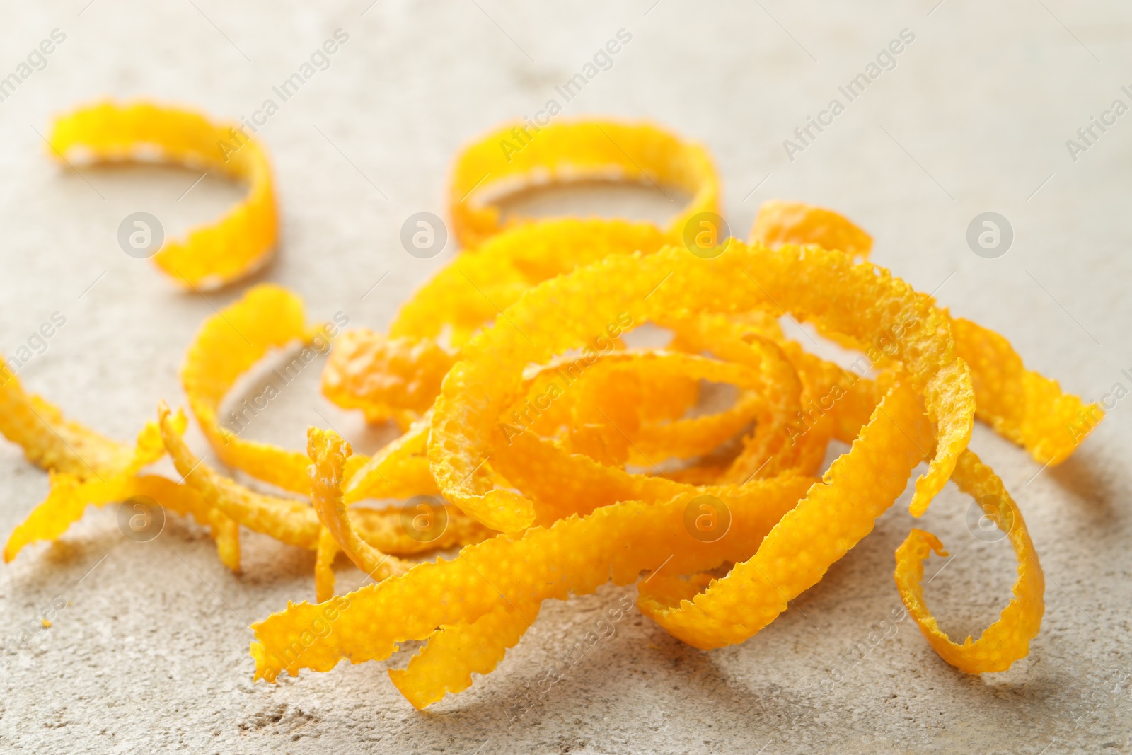 Photo of Pile of fresh orange zest on light textured table, closeup