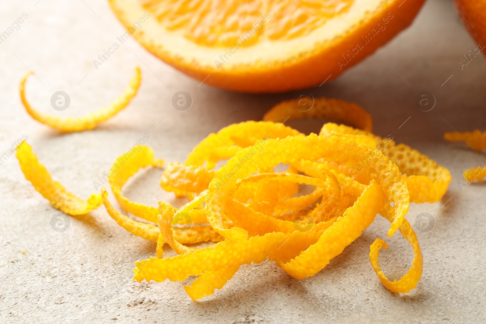 Photo of Pile of fresh orange zest on light textured table, closeup