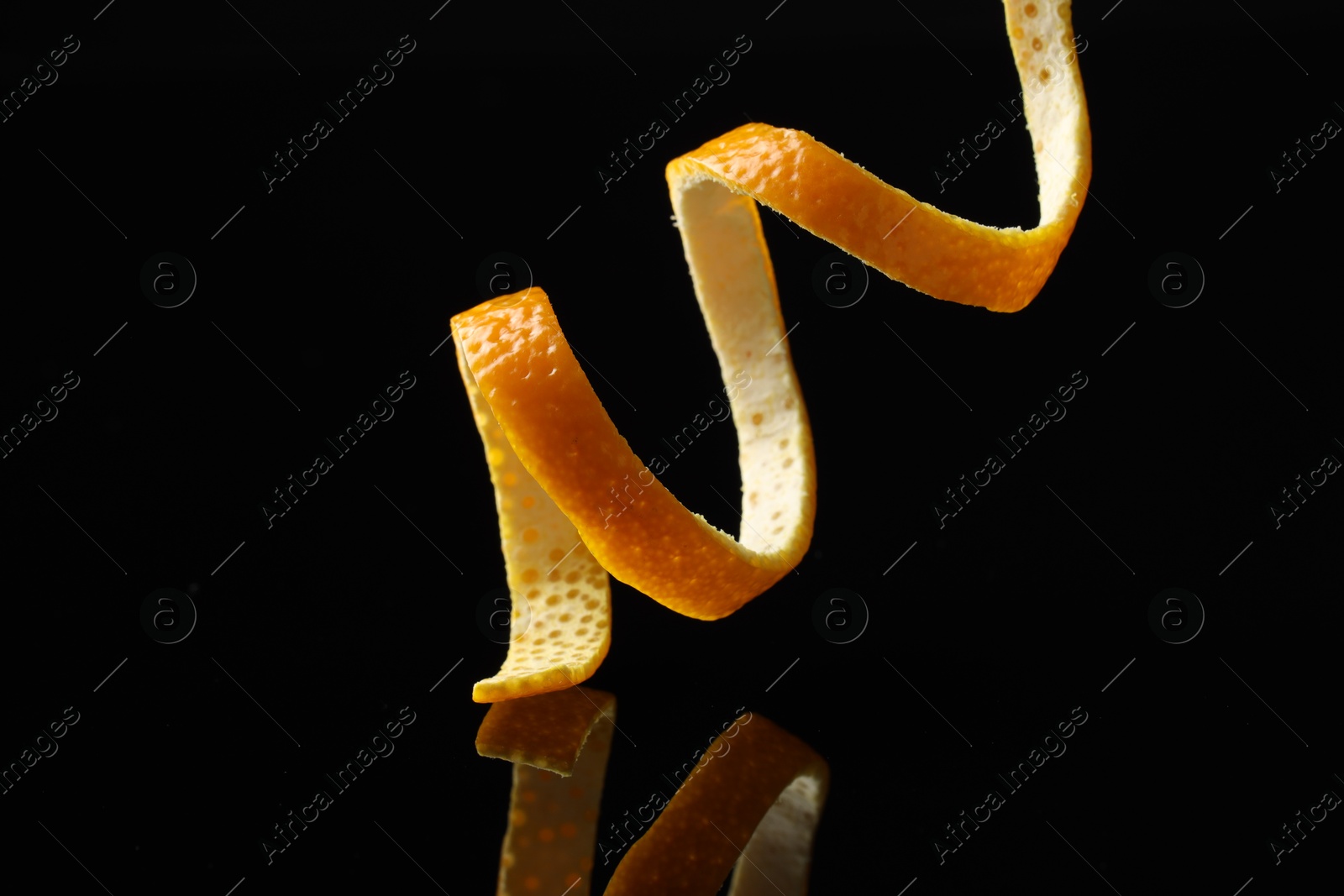 Photo of One fresh orange peel on black mirror surface, closeup