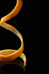 Photo of One fresh orange peel on black mirror surface, closeup. Space for text