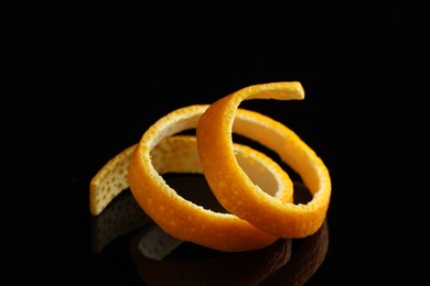 Photo of One fresh orange peel on black mirror surface, closeup