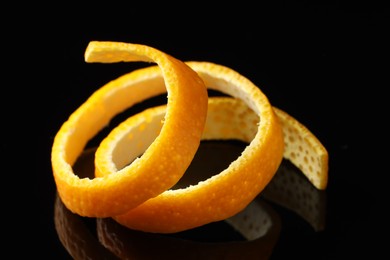 Photo of One fresh orange peel on black mirror surface, closeup