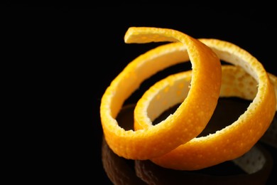 Photo of One fresh orange peel on black mirror surface, closeup. Space for text