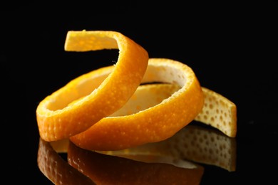 Photo of One fresh orange peel on black mirror surface, closeup