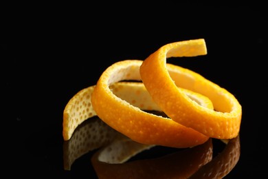 Photo of One fresh orange peel on black mirror surface, closeup