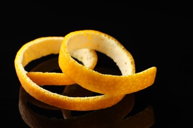 Photo of One fresh orange peel on black mirror surface, closeup