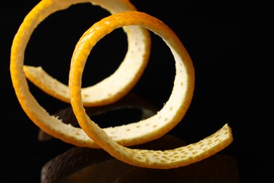 Photo of One fresh orange peel on black mirror surface, closeup