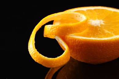 Photo of Fresh orange peel and half of fruit on black mirror surface, closeup