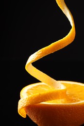 Photo of Fresh orange peel and half of fruit on black background, closeup