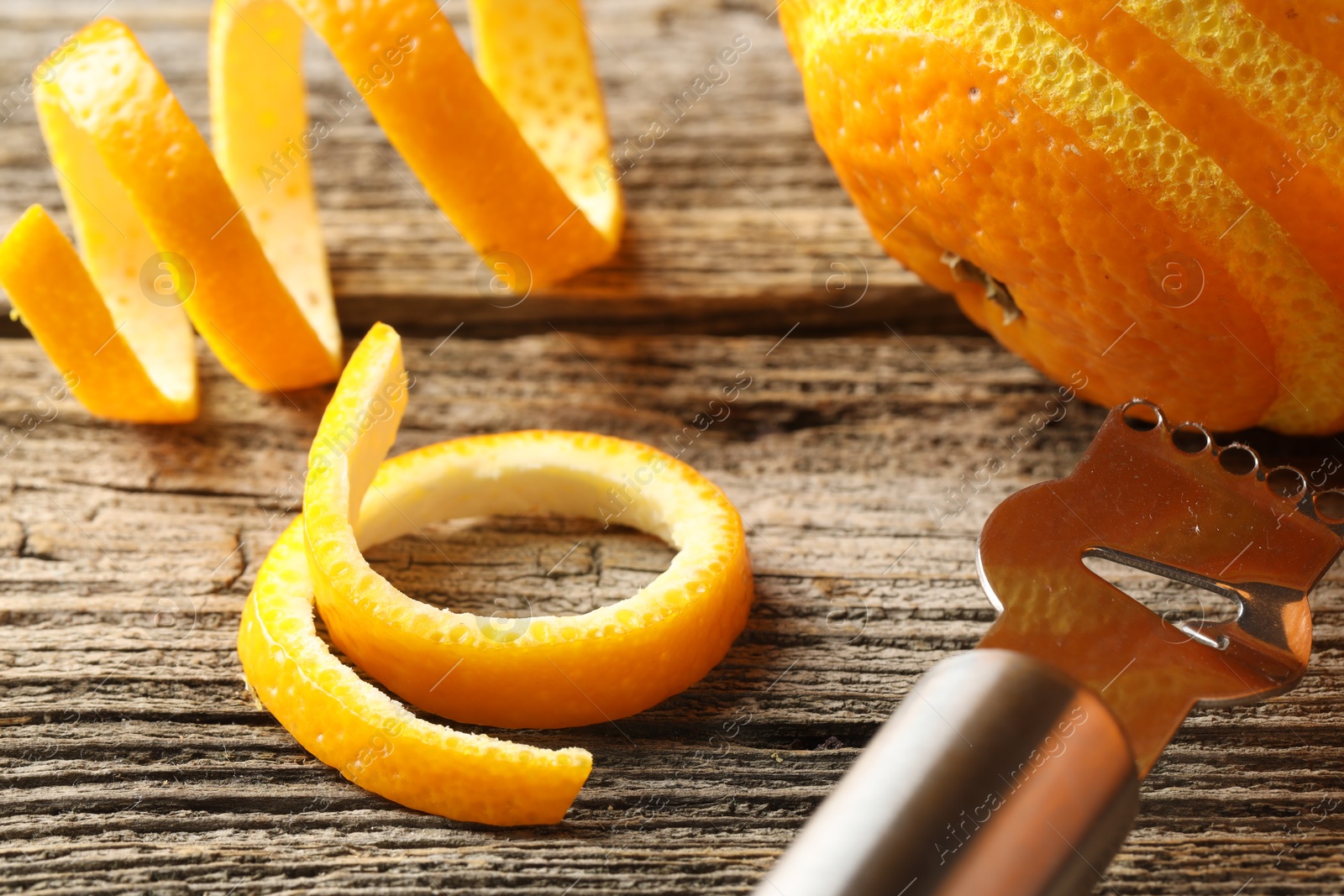 Photo of Fresh orange peels, fruit and zester on wooden table, closeup