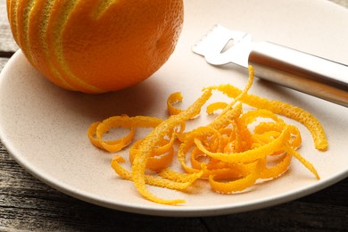 Photo of Fresh orange zest, fruit and zester on wooden table, closeup