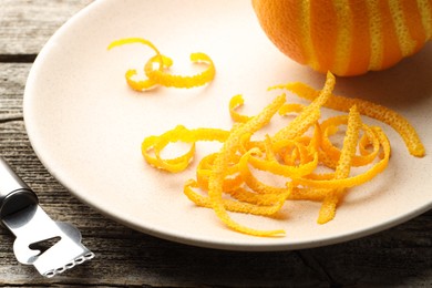 Fresh orange zest, fruit and zester on wooden table, closeup