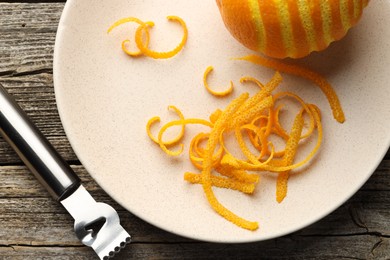 Photo of Fresh orange zest, fruit and zester on wooden table, flat lay