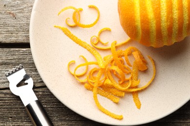 Photo of Fresh orange zest, fruit and zester on wooden table, flat lay